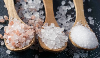 Farklı tuz türleri. Deniz, Himalaya ve mutfak tuzu. Siyah arka planda üç tahta kaşığın üst görüntüsü