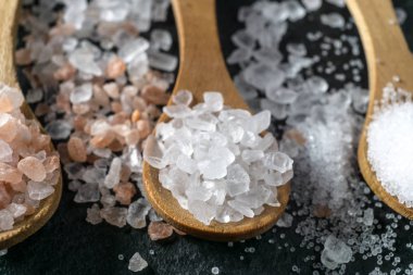 Farklı tuz türleri. Deniz, Himalaya ve mutfak tuzu. Siyah arka planda üç tahta kaşığın üst görüntüsü