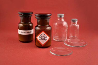 Zehirli görüntüler şişesi. Piktogram görüntüleriyle dolu bir şişe. Laboratuvar aksesuarları görüntüleri. Kırmızı arka planda şişeler. Kahverengi cam kaplar. Kahverengi kimyasal cam deposu fotoğrafı.