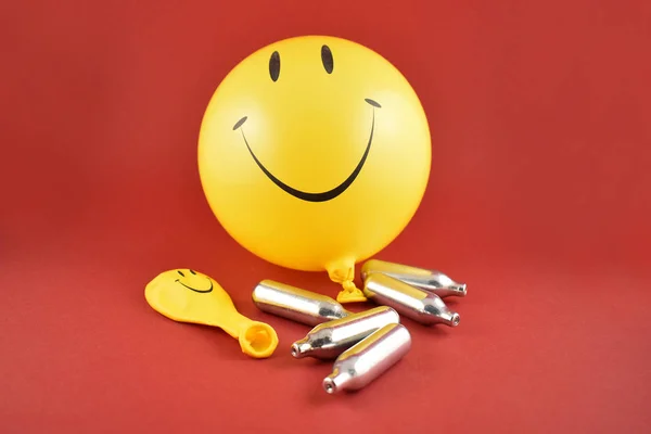 Laughing gas bombs stock photo images. Laughing gas balloons. Happy emoji balloon. Smiley inflatable balloon isolated on a red background. Laughing party balloon. Nitrous oxide bulbs