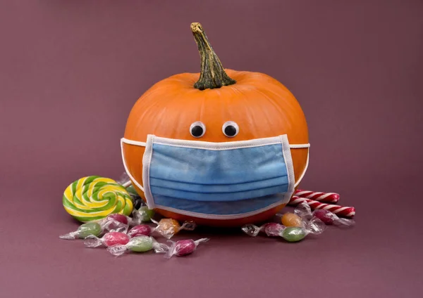 Hallowee pumpkin with protective mask and candies stock images. Funny halloween pumpkin with coronavirus mask and pile of sweets photo. Pumpkin wearing medical mask on face to prevent flu images