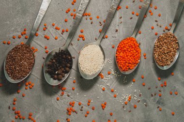 Süper yiyecekli kaşıklar - keten tohumu, susam, biber, kırmızı mercimek, gri arka planda karabuğday.