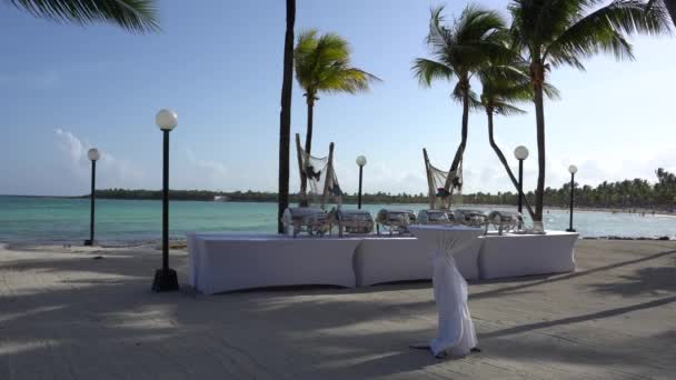 Blick auf den Strand des Luxushotels an der tropischen Küste. Blätter von Kokospalmen flattern im Wind gegen den blauen Himmel. Vorbereitung auf das Galadinner. türkisfarbenes Wasser der karibischen Riviera Maya Mexico — Stockvideo