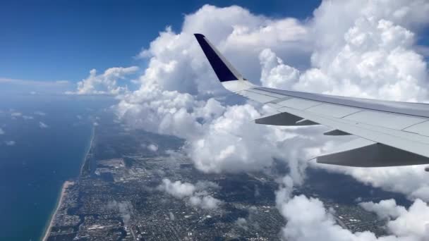 A sobrevoar Miami. Vista da costa leste da janela dos aviões. Lindas nuvens brancas contra o céu azul. As águas azul-turquesa da costa atlântica. — Vídeo de Stock
