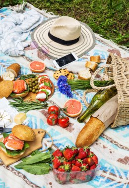 Sepet, sandviç, meyve, çilek, salata ve zeytin ile çimlerde piknik ayarı.