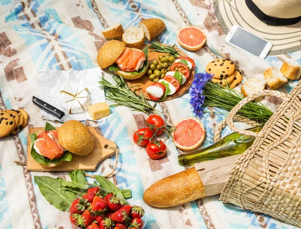 Sepet, sandviç, meyve, çilek, salata ve zeytin ile çimlerde piknik ayarı.
