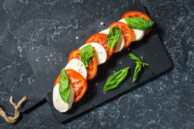 Caprese salatası. Taş masa üzerinde mozzarella peyniri, domates ve fesleğen bitki yaprakları.