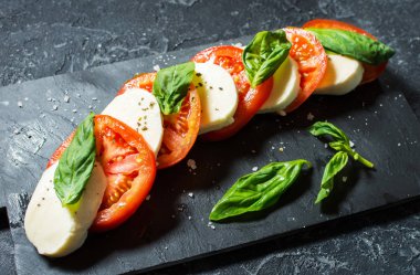 Caprese salatası. Taş masa üzerinde mozzarella peyniri, domates ve fesleğen bitki yaprakları.