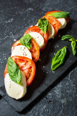 Caprese salatası. Taş masa üzerinde mozzarella peyniri, domates ve fesleğen bitki yaprakları.