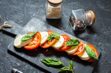 Caprese salatası. Taş masa üzerinde mozzarella peyniri, domates ve fesleğen bitki yaprakları.