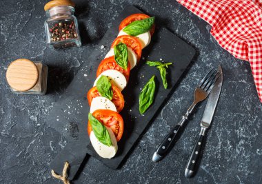Caprese salatası. Taş masa üzerinde mozzarella peyniri, domates ve fesleğen bitki yaprakları.