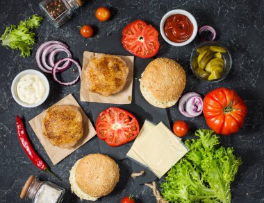 Yemek hamburger için malzemeler. Izgara tavuk patty, çörekler, soğan, domates, turşu, sos, peynir üzerinde siyah arka plan üstten görünüm