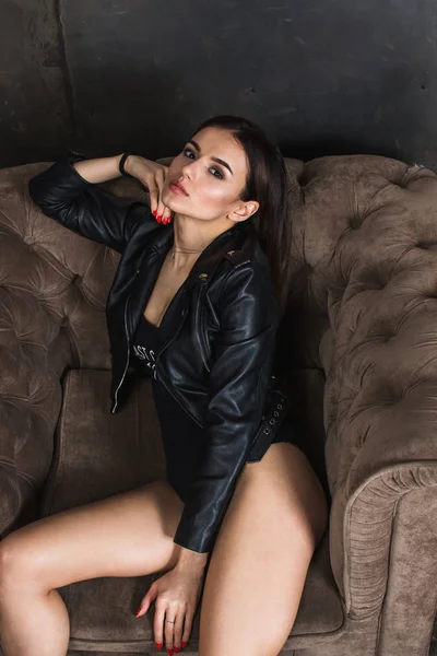 ソファに座って黒い革のジャケットでゴージャスな美しいセクシーな女性 — ストック写真