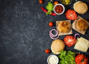 Yemek hamburger için malzemeler. Izgara tavuk patty, çörekler, soğan, domates, turşu, sos, peynir üzerinde siyah arka plan üstten görünüm
