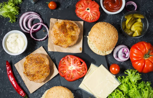 Yemek hamburger için malzemeler. Izgara tavuk patty, çörekler, soğan, domates, turşu, sos, peynir üzerinde siyah arka plan üstten görünüm