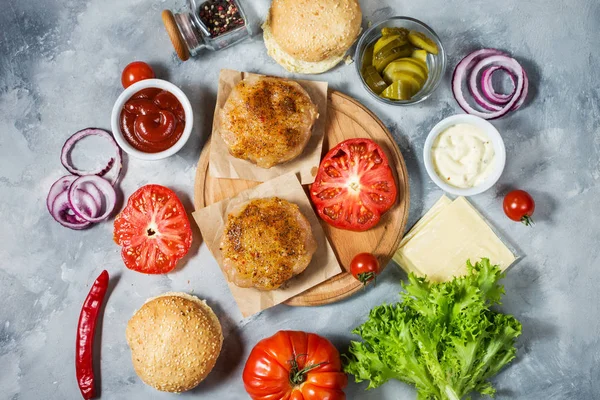 Yemek hamburger için malzemeler. Izgara tavuk patty, çörekler, soğan, domates, turşu, sos, peynir üzerine beton arka plan üstten görünüm