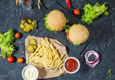 İki biftek Burger, patates kızartması patates ve salatalık karanlık taş masada. Üstten görünüm