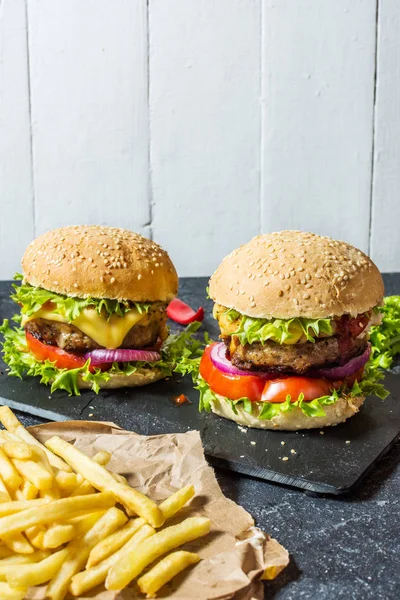 İki biftek Burger, patates kızartması patates ve salatalık karanlık taş masada.