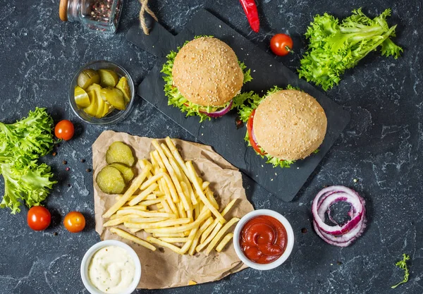İki biftek Burger, patates kızartması patates ve salatalık karanlık taş masada. Üstten görünüm
