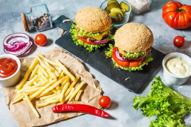 İki biftek Burger, patates kızartması patates ve salatalık beton masada.