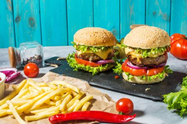 İki biftek Burger, patates kızartması patates ve salatalık beton masada.