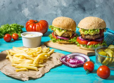 İki biftek Burger, patates kızartması patates ve salatalık mavi ahşap masa üzerinde.