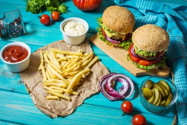 İki biftek Burger, patates kızartması patates ve salatalık mavi ahşap masa üzerinde.