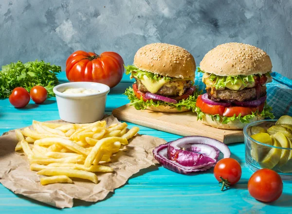 İki biftek Burger, patates kızartması patates ve salatalık mavi ahşap masa üzerinde.