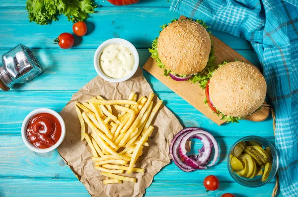 İki biftek Burger, patates kızartması patates ve salatalık mavi ahşap masa üzerinde. Üstten görünüm