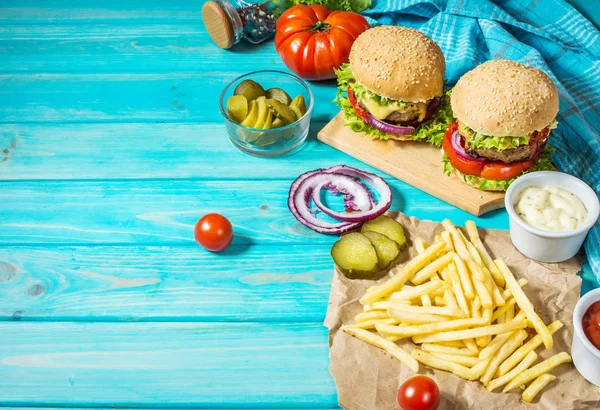 İki biftek Burger, patates kızartması patates ve salatalık mavi ahşap masa üzerinde. Kopya alanı