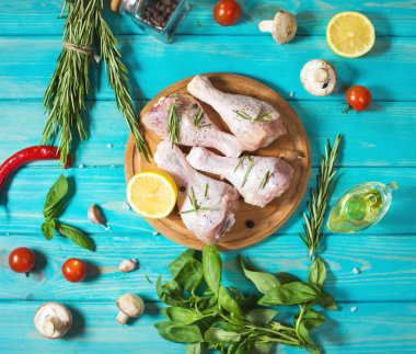 Ham pişmemiş tavuk budu, mavi ahşap arka plan, et yemek pişirmek için malzemelerle sopaları. Üstten görünüm