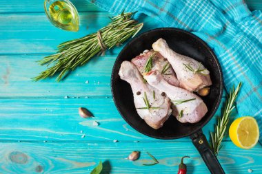 Ham pişmemiş tavuk budu, mavi ahşap arka plan, et yemek pişirmek için malzemelerle sopaları. En iyi görünüm ve kopya alanı