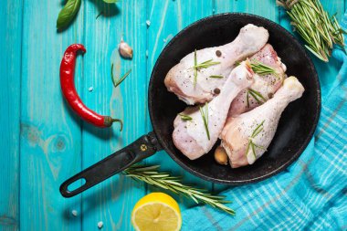 Ham pişmemiş tavuk budu, mavi ahşap arka plan, et yemek pişirmek için malzemelerle sopaları. Üstten görünüm