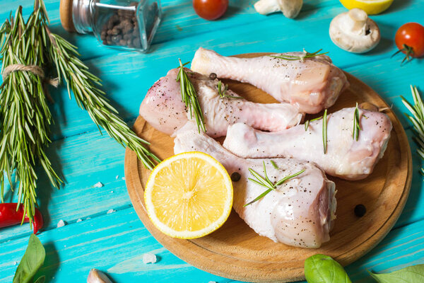 Raw uncooked chicken legs, drumsticks on blue wood background, meat with ingredients for cooking