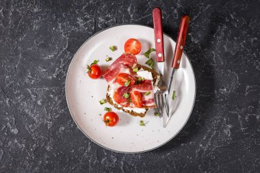 Kiraz domates ve plaka taş koyu arka plan üzerinde prosciutto ile sandviç. Üstten görünüm