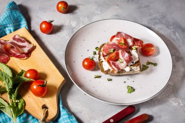 Kiraz domates ve beton arka plan üzerinde plaka üzerinde prosciutto ile sandviç.