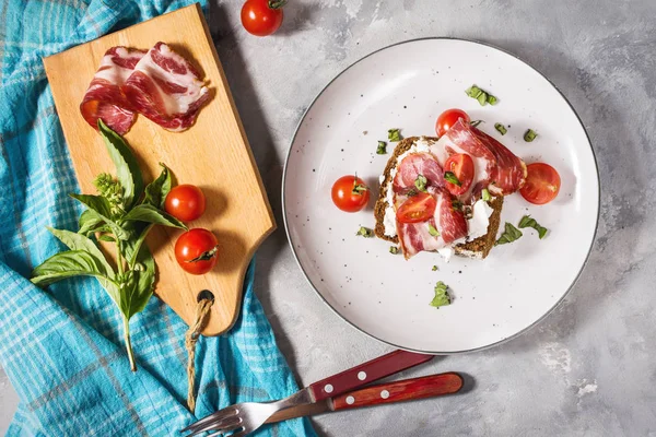 Sandwich with cherry tomatoes and prosciutto on plate over concrete background. Top view