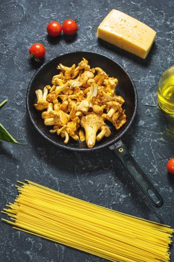 Karanlık taş arka plan üzerinde pişmemiş makarna ve Cantharellus cibarius mantar.