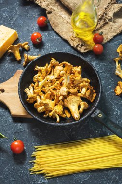 Karanlık taş arka plan üzerinde pişmemiş makarna ve Cantharellus cibarius mantar