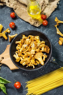 Pişmemiş makarna ve Cantharellus cibarius taş koyu arka plan üzerinde mantar. Üstten görünüm.