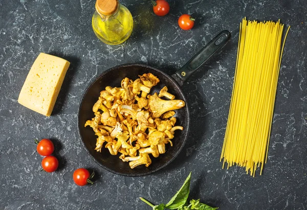 Pişmemiş makarna ve Cantharellus cibarius taş koyu arka plan üzerinde mantar. Üstten görünüm.