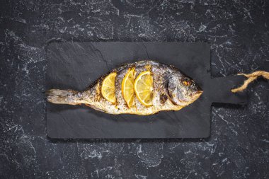 Koyu arka plan, üstten görünüm üzerinde limonlu taş plaka üzerinde ızgara balık