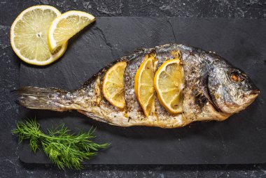 Koyu arka plan, üstten görünüm üzerinde limonlu taş plaka üzerinde ızgara balık