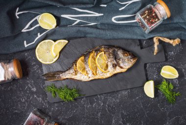 Koyu arka plan, üstten görünüm üzerinde limonlu taş plaka üzerinde ızgara balık