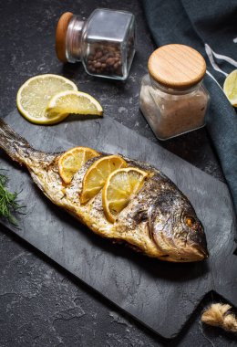 Koyu arka plan üzerinde limonlu taş plaka üzerinde ızgara balık