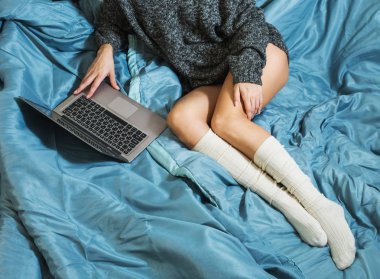 Seksi bacaklar ile bir dizüstü bilgisayar yatakta yatıyordu bir sıcak kazaklı genç bir kızla. Evde çalışıyorum. Üstten görünüm