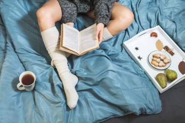 Yatakta, bir fincan çay ve bir kitap okuma ile kız güzel bacaklar yakın çekim