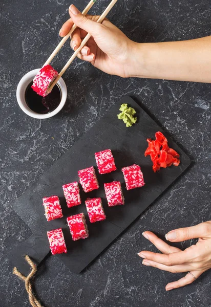 Hand with chopsticks on sushi set with soy sauce on black stone desk. Top view