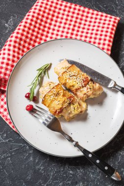 Doldurulmuş tavuk göğsü pastırma taş masada bir plaka üzerinde sarılı.