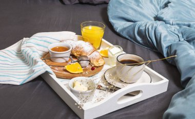 Kahve, kruvasan ve portakal suyu beyaz tepsi ile yatakta kahvaltı.